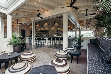 The interior of a restaurant with black and white patterned sofa cushions and small round seats and tables.