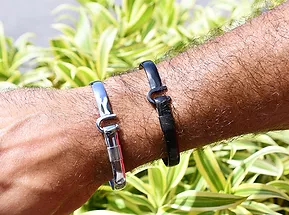 Silver color and black color hook bracelets on a wrist in front of leaves