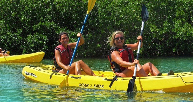 Two women paddle a yellow kayak in the ocean in the mangroves