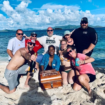 A group of people pose on a beach with a treasure chest