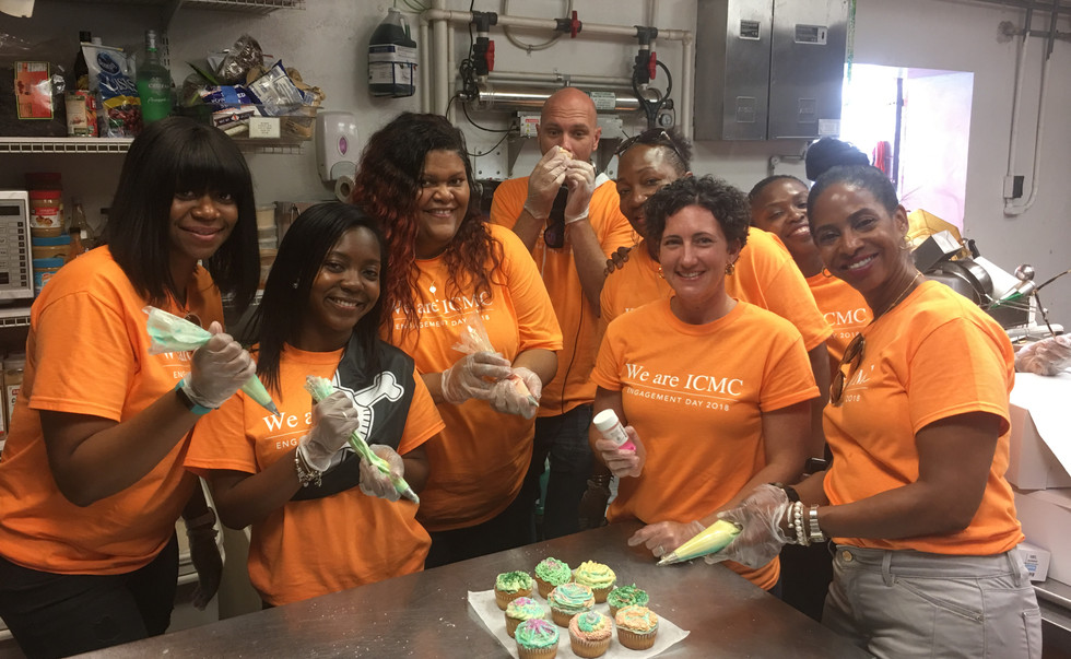 8 people in orange t shirts pose while frosting cupcakes.