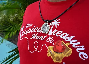 An authentic pirate coin on a leather necklace sits on the chest of a person wearing a Tropical Treasure Hunt rash guard