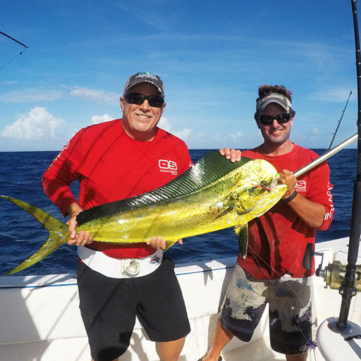 Two men pose on the deck of a boat holding a large fish