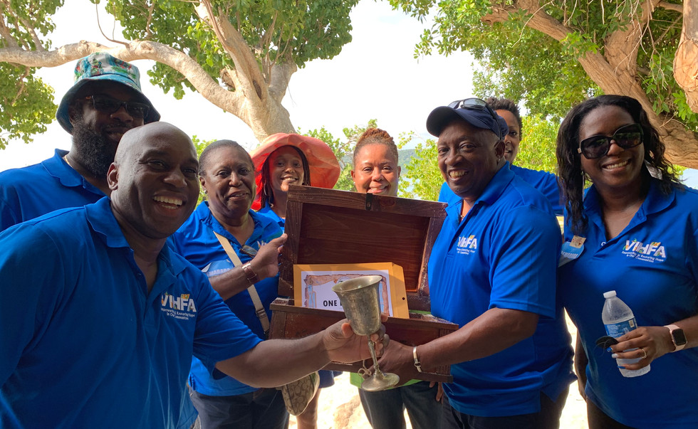 8 people in blue polo shirts with the VIHFA logo embroidered on the left breast pocket side pose among the mangroves with their treasure. They are holding an open treasure chest with a gift certificate inside and a gold goblet.