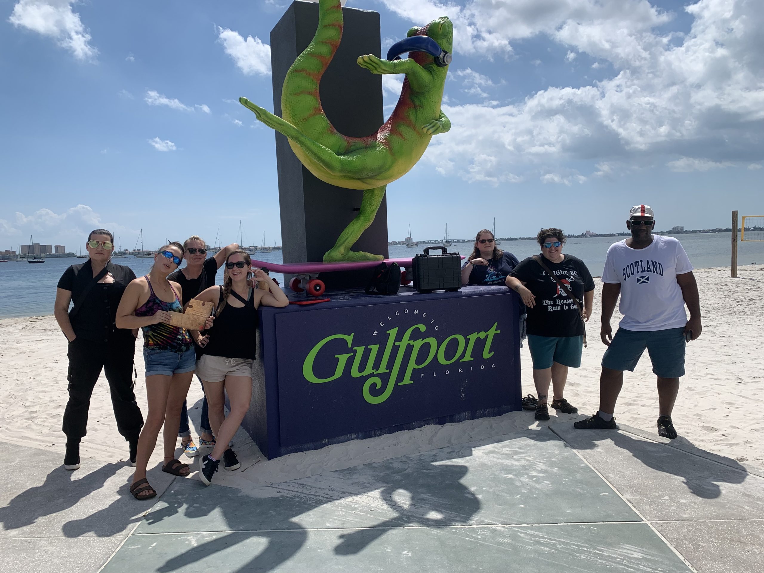 Group of people standing on a beach next to a large sign that says Gulfport topped with a lizard
