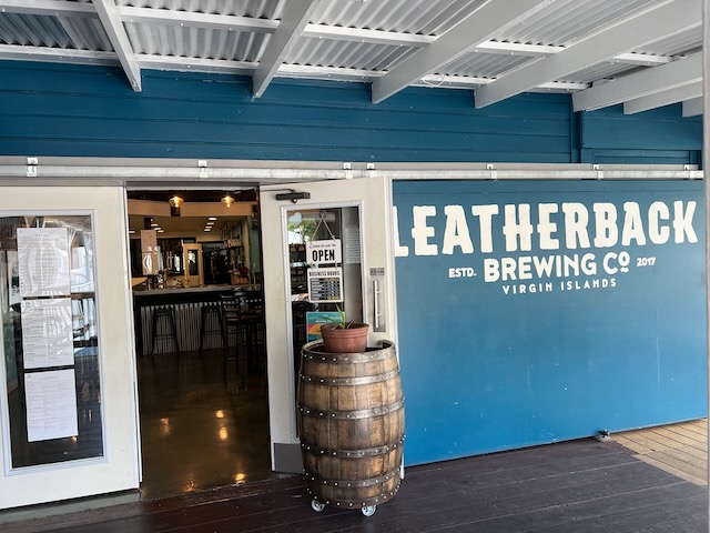 Exterior looking into Leatherback Brewery. Visible is a wooden barrel holding open the door, a bar, and some bar stools