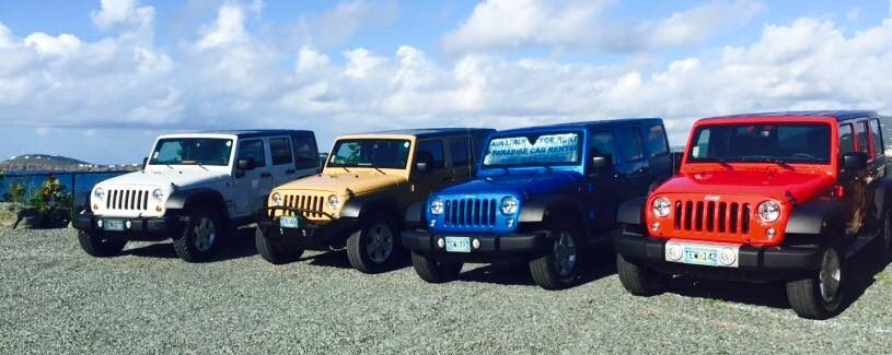 Four Jeeps (white, gold, blue, red) sit in a parking lot with the ocean behind them.