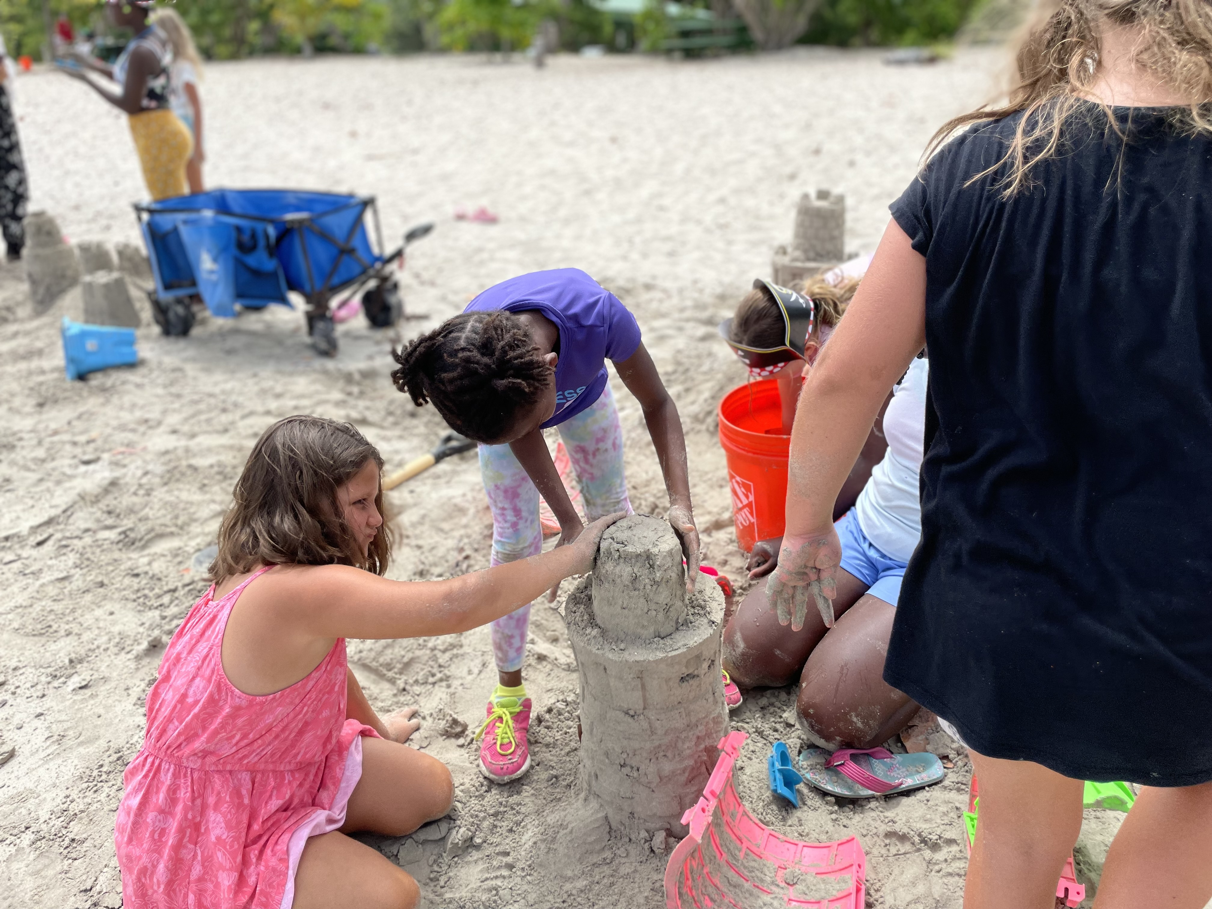 Two girls work together to pat down the final tower of a sandcastle.