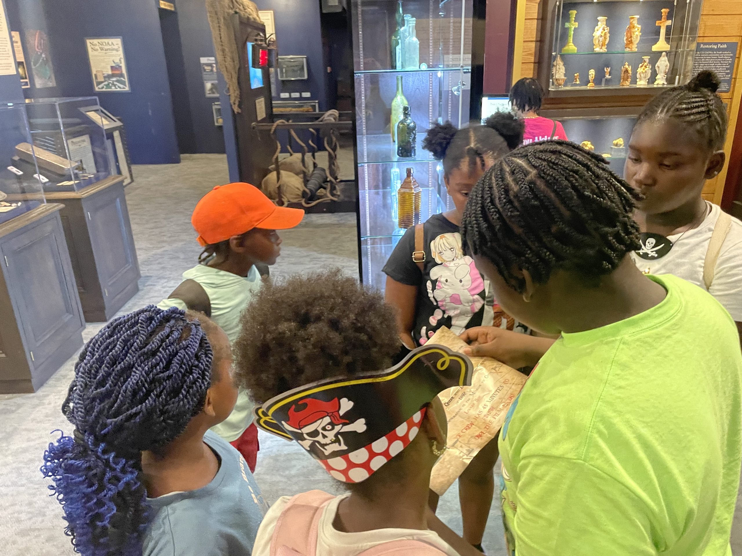 A group of children stand in a circle looking at a glossy piece of paper with questions on it.